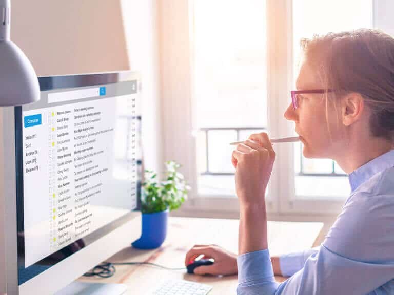 Woman working at a computer, checking emails on a large monitor in a bright office